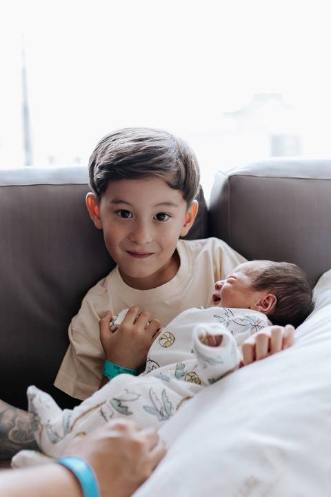 Foto do irmão mais velho sorrindo ao lado do bebê.'