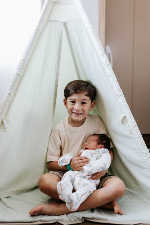 Foto do irmão mais velho com o bebê em tenda decorativa.'