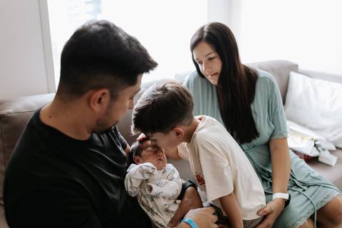 Foto do irmão mais velho interagindo com o bebê no colo do pai.'