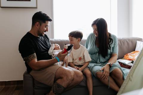 Foto da família sentada no sofá com o recém-nascido.'