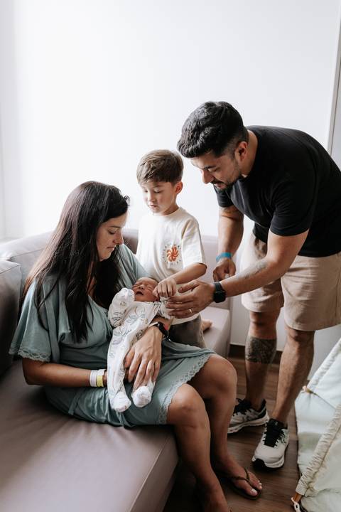 Foto do encontro do irmão mais velho conhecendo o recém-nascido no hospital.'