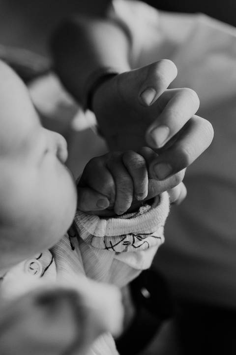 Foto em preto e branco do detalhe da mão do bebê com a mão do irmão. '