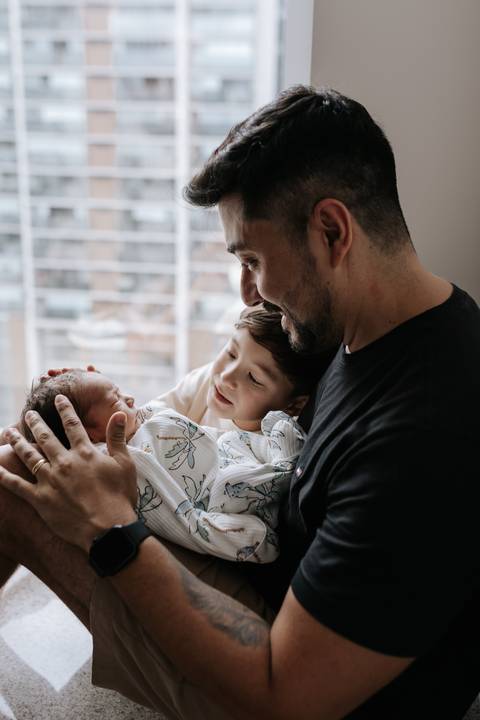 Foto do pai e do filho mais velho observando o bebê.'