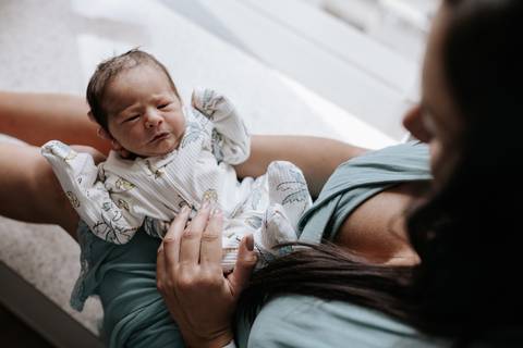 Foto da mãe segurando o bebê no colo no quarto. '
