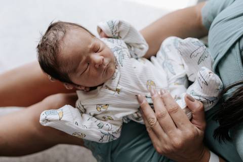 Foto da mãe com o bebê apoiado em sua mão. '