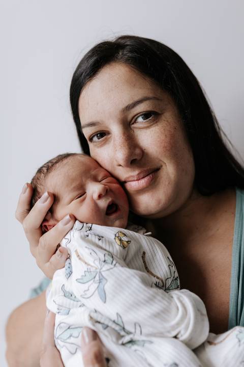 Foto aproximada da mãe segurando o recém-nascido no colo.'