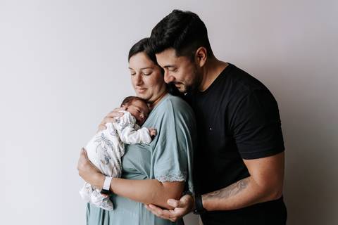 Foto do casal abraçado com o recém-nascido na maternidade.'