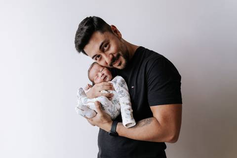 Foto do pai sorrindo com o bebê no colo.'