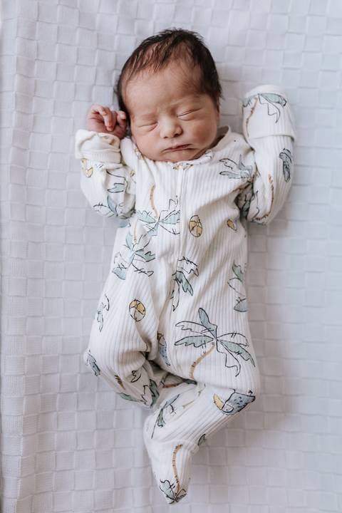 Foto aproximada do bebê dormindo com os braços pra cima. '