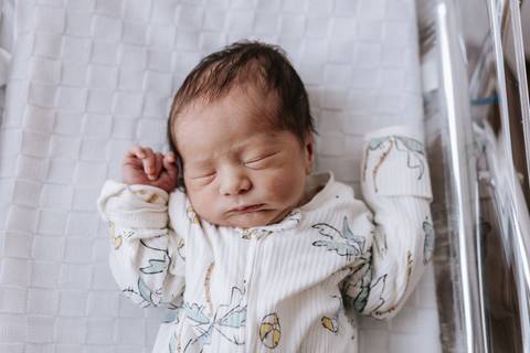 Foto do recém-nascido dormindo no berço hospitalar.'