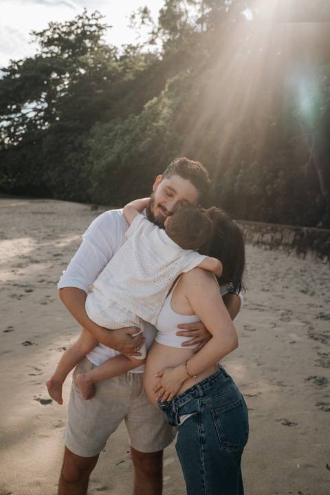 Foto da família abraçada durante ensaio externo no litoral.'