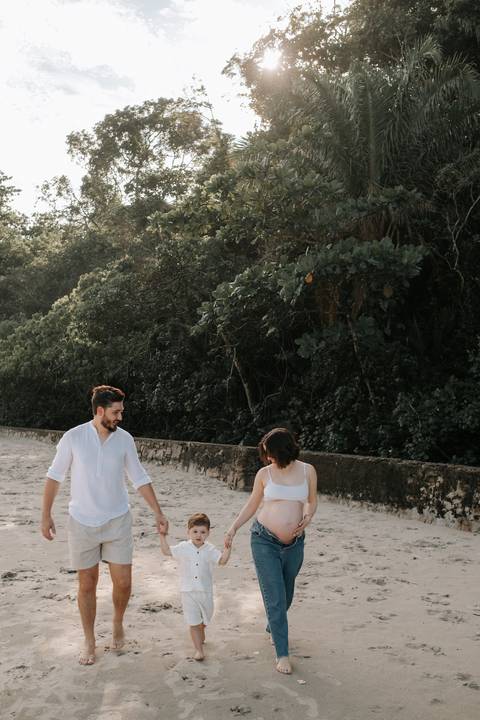 Foto da família caminhando na praia durante o ensaio gestante.'