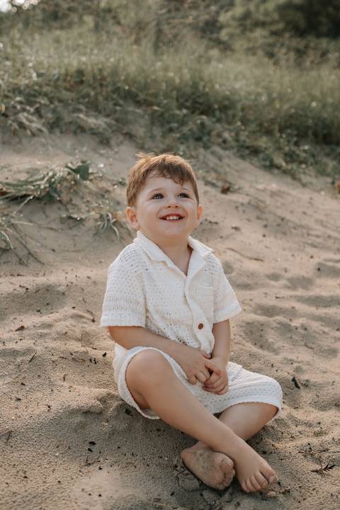Foto aproximada do filho sorrindo sentado na areia.'