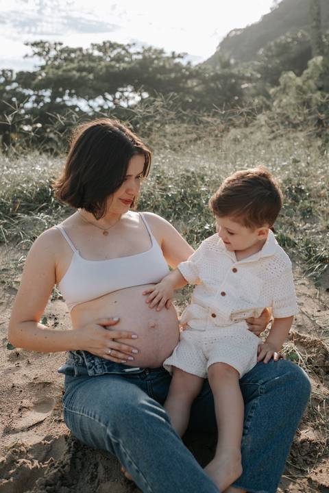 Foto da gestante com o filho observando a barriga de grávida.'