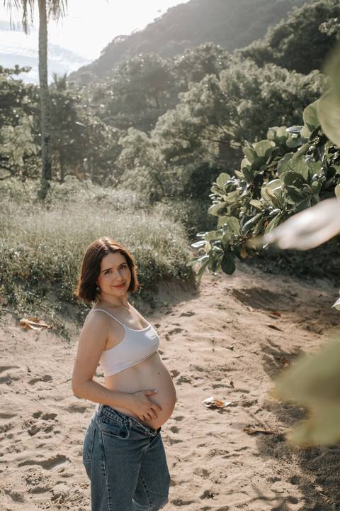 Foto da gestante em meio à vegetação da praia.'