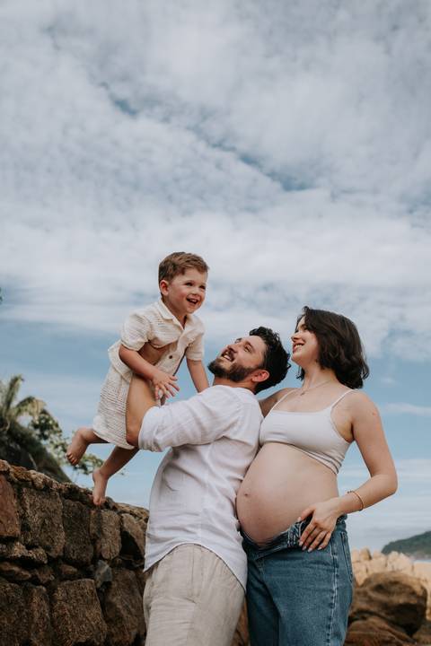 Foto do pai brincando com o filho na areia com a mão ao lado.'