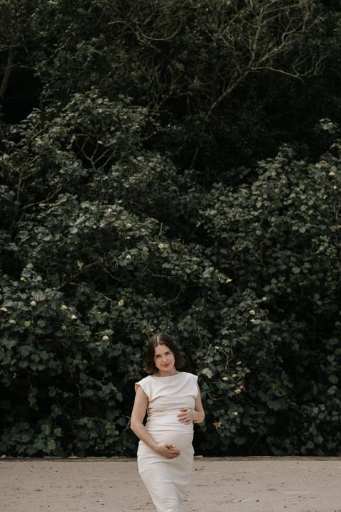 Foto da gestante em meio à vegetação natural da praia.'