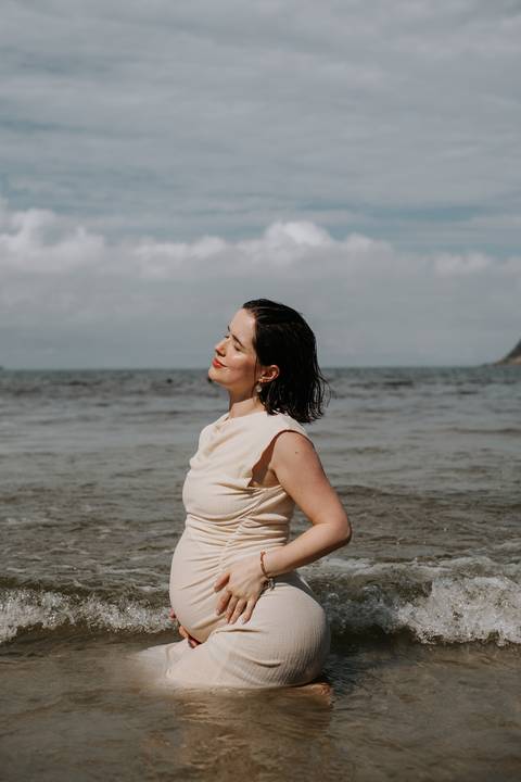 Foto da gestante de perfil na beira do mar. '