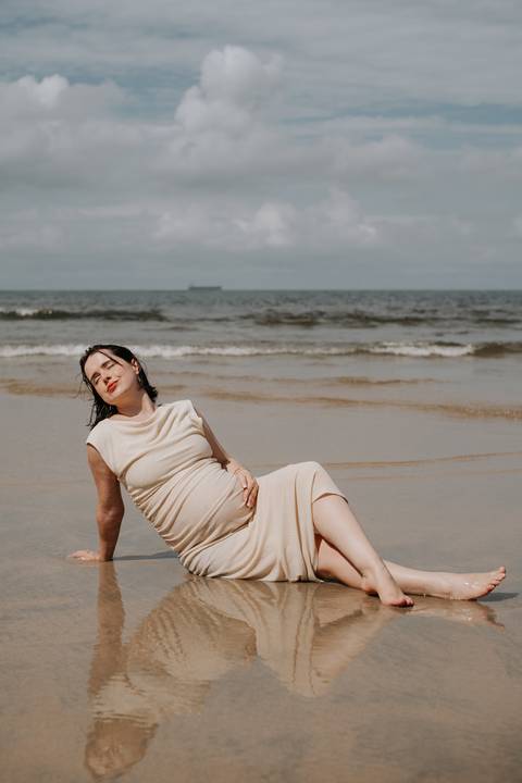 Foto da gestante sentada na areia com a mãe na barriga. '