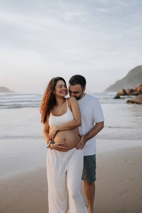 Foto do pai beijando o ombro da gestante em momento de carinho.'