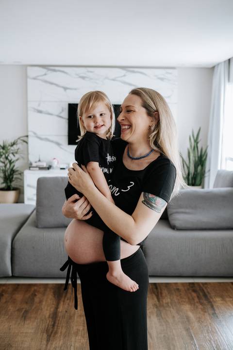 Foto da gestante sorrindo com a filha mais velha no colo.'