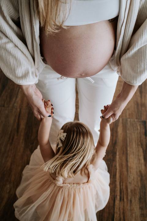 Foto em ângulo superior do detalhe das mãos da mãe e da filha entrelaçadas. '