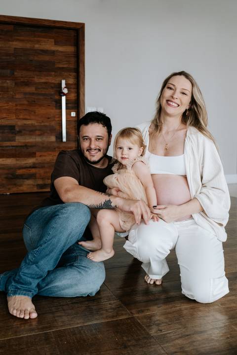 Foto da família sentada no chão com a barriga de grávida em destaque.'