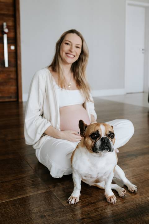Foto da gestante sentada no chão com o cachorro de estimação.'