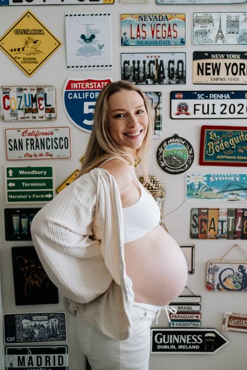 Foto de perfil da gestante em frente a parede decorada com placas.'