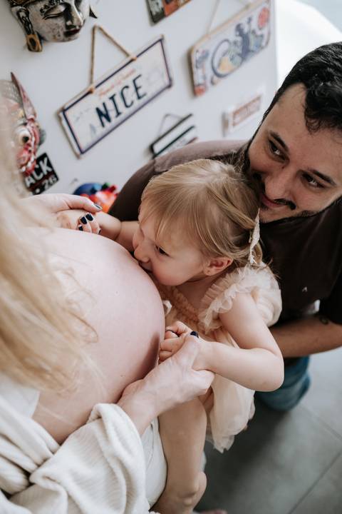 Foto da filha mais velha beijando a barriga de grávida da mãe.'