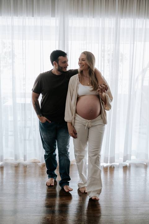 Foto do casal de mãos dadas em frente à cortina no ensaio lifestyle.'