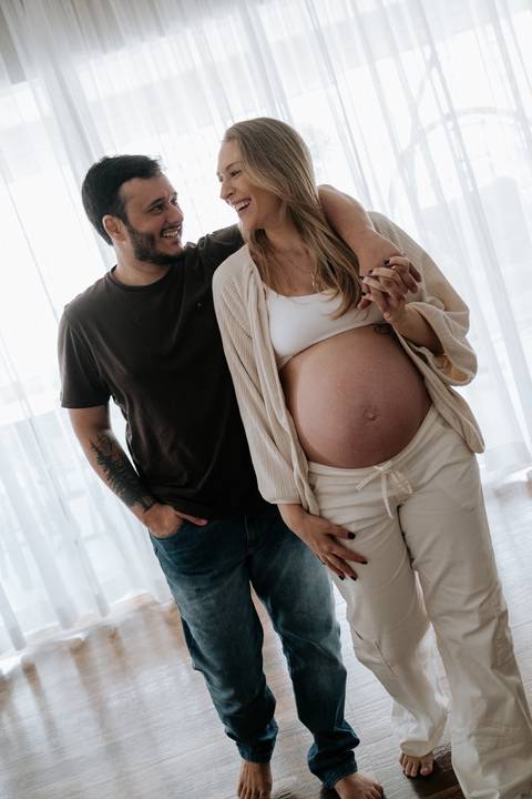 Foto do casal trocando carinho e destacando a barriga de grávida.'