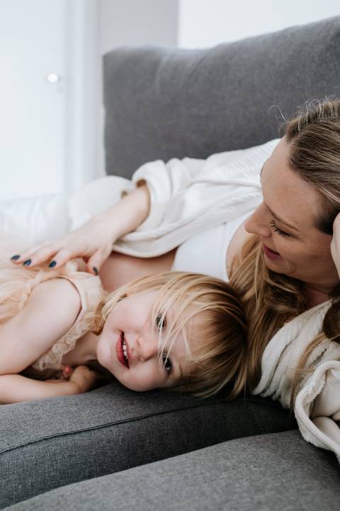 Foto da gestante deitada no sofá com a filha pequena ao seu lado.'