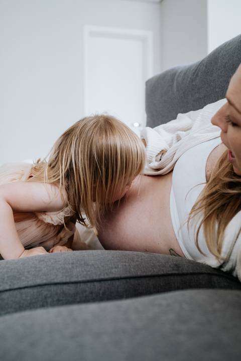 Foto da filha mais velha dando um beijo carinhoso na barriga da mãe.'