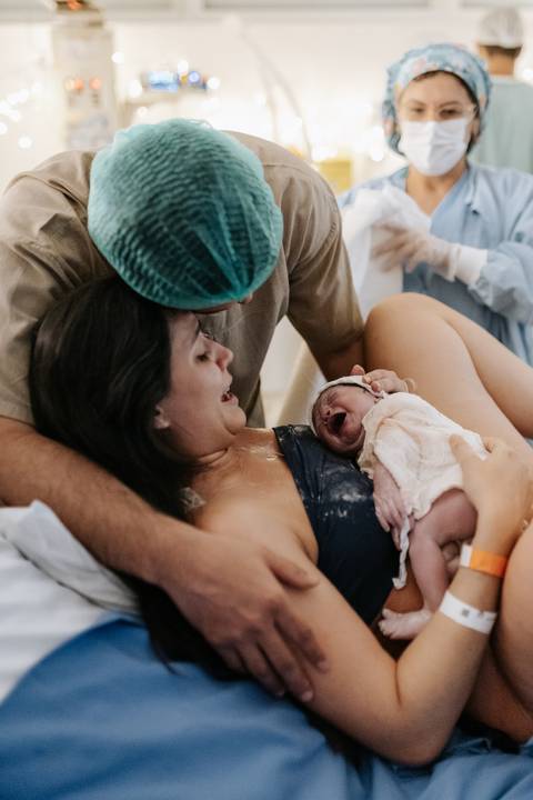 Foto da mãe emocionada recebendo o recém-nascido no colo.'