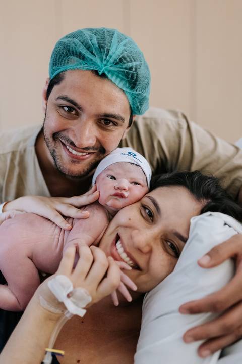 Foto da família sorrindo unida com o bebê nos primeiros minutos de vida.'