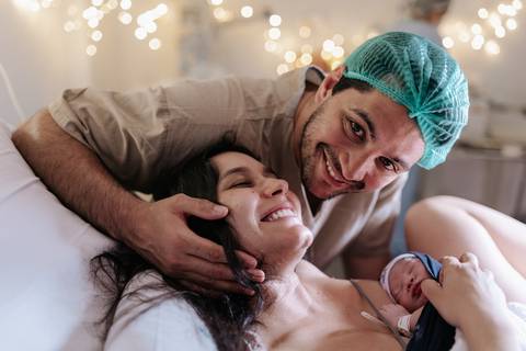 Foto da família reunida e sorridente com o recém-nascido na sala de parto.'