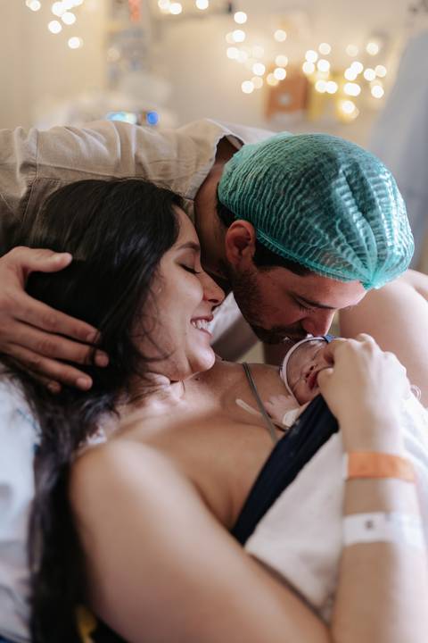 Foto do casal beijando o recém-nascido logo após o parto.'