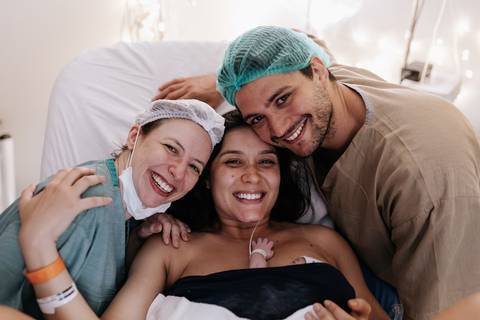 Foto da família posando com a enfermeira na sala de parto.'