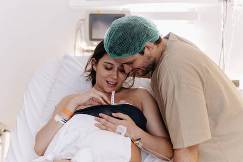 Foto da mãe com o bebê no colo e o pai ao lado.'