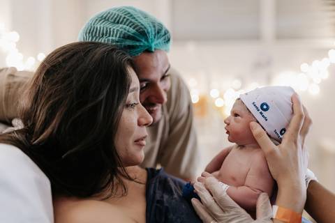 Foto do pai e da mãe emocionados observando o bebê na sala de parto.'