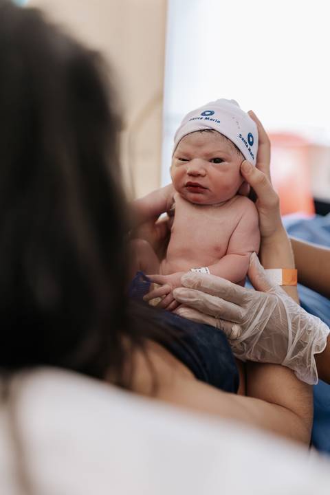 Foto aproximada do recém-nascido sendo segurado pela mãe.'