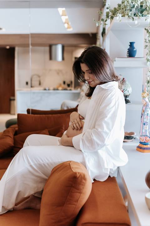 Foto da gestante sentada no sofá acariciando a barriga de grávida.'