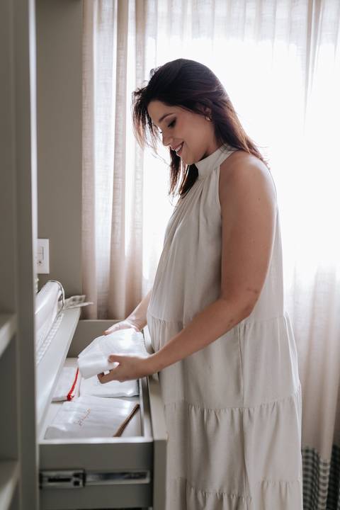 Foto da gestante organizando as roupinhas no berço do bebê.'