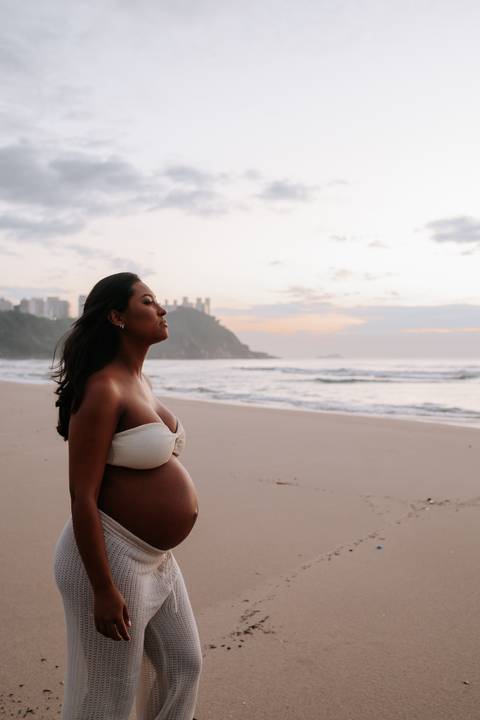 Foto da gestante de perfil com os olhos fechados apreciando o amanhecer na praia.'