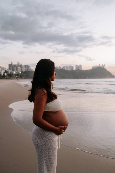 Foto da gestante observando o mar durante o ensaio no nascer do sol.'
