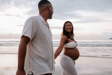 Foto do casal caminhando e sorrindo durante ensaio externo na praia.'