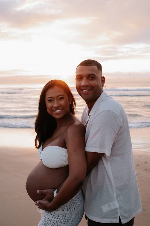 Foto aproximada do casal sorrindo com o mar ao fundo.'
