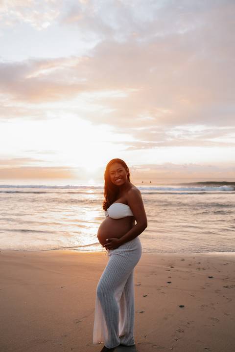 Foto da gestante sorrindo com a luz dourada do sol refletida na água.'