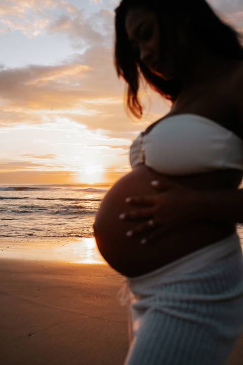 Foto em detalhe da barriga de grávida com o sol ao fundo.'